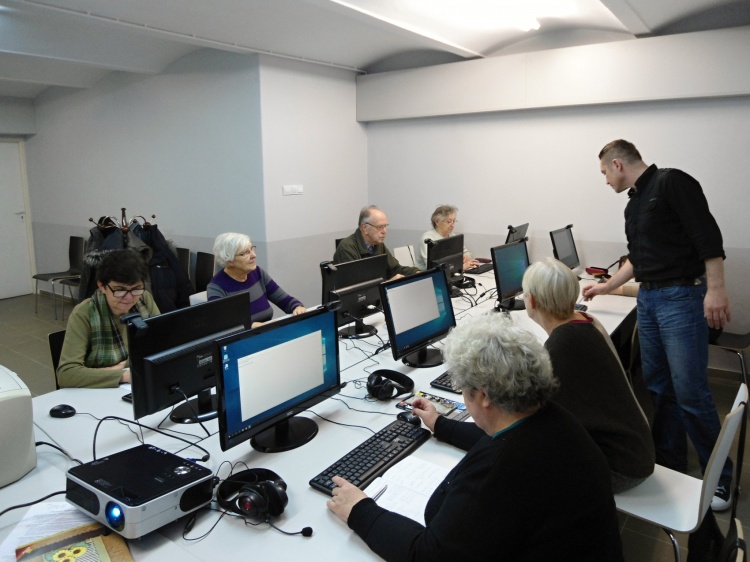 Widok ogólny na kurs, seniorzy przy komputerach i stoi instruktor