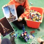 Dziewczynka trzyma zdjęcie wieży Eiffla i jego model wieży z klocków lego