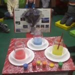 Materiały - trzy słoiki na stole z kolorowymi płynami i farby