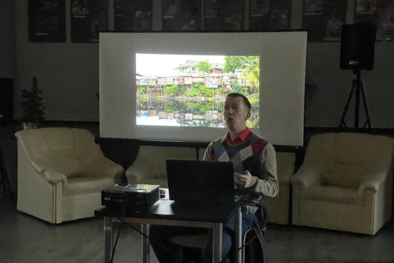 Tomasz Burdzik, na tle na ekranie zdjęcie wioski z Borneo