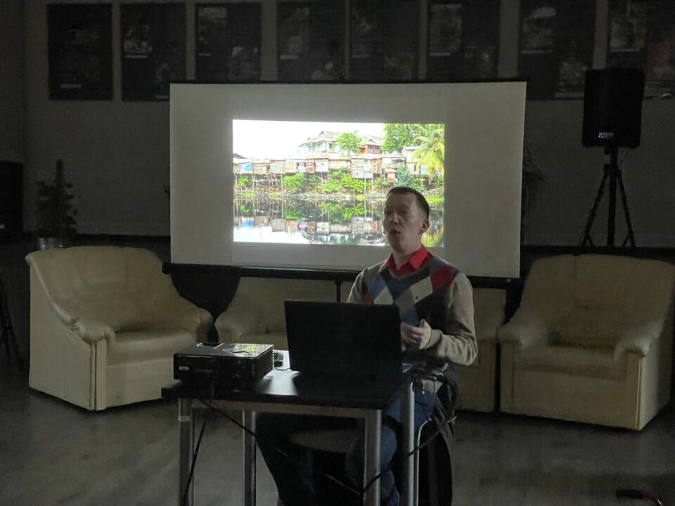Tomasz Burdzik, na tle na ekranie zdjęcie wioski z Borneo