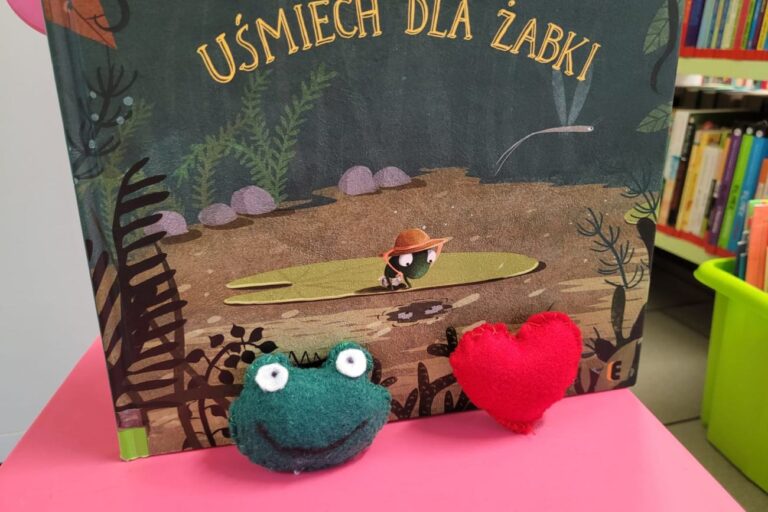 Głowa żaby i serce z filcu i w tle książka - Uśmiech dla żaby