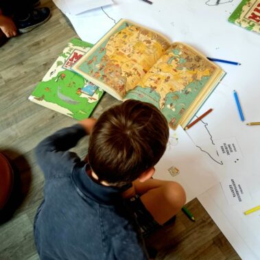 Otwarta książka z mapą, chłopiec dokonuje wyboru do swojej pracy plastycznej