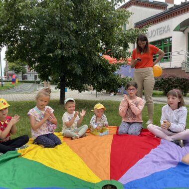 Dzieci siedzą na dużej kolorowej płachcie