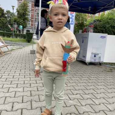 Chłopiec jako Indianin, na głowie opaska z piórami, w ręku trzyma mały totem