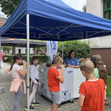 Dzieci gromadzą i piją wodę koło stoiska PWiK
