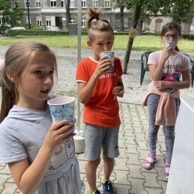 Trzy dziewczynki piją napój przy stoisku PWiK