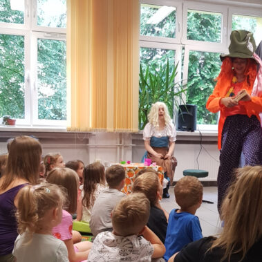 Dzieci siedzą na podłodze i słuchają przestawienia na scenie z Kapelusznikiem