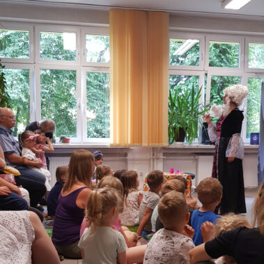 Dzieci siedzą na podłodze i słuchają przestawienia na scenie z aktorką