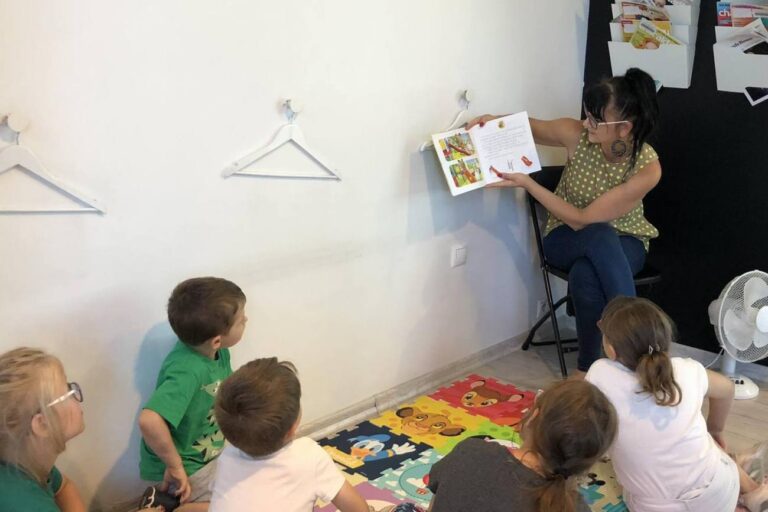 Bibliotekarka głośno czyta, dzieci siedzą na piankowym dywanie
