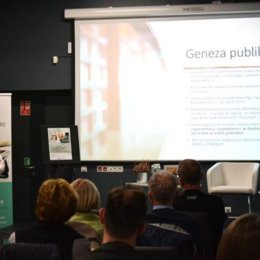 Leszek Jodliński stoi koło ekranu, na ekranie wyświetla genezę publikacji