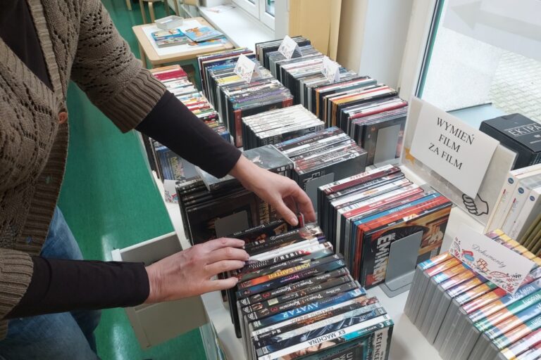 Na stole leżą uporządkowane filmy na DVD i ktoś wybiera sobie filmy.