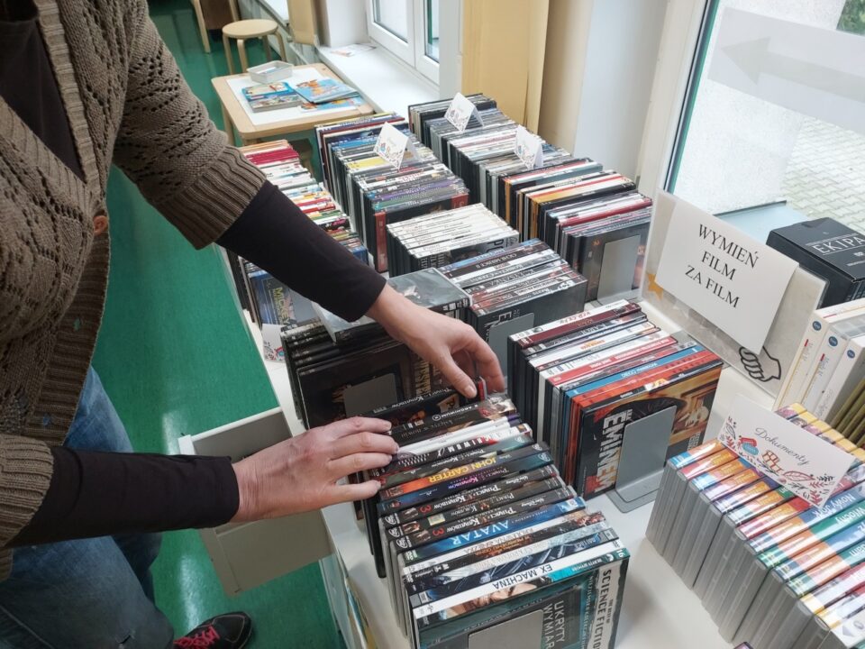 Na stole leżą uporządkowane filmy na DVD i ktoś wybiera sobie filmy.