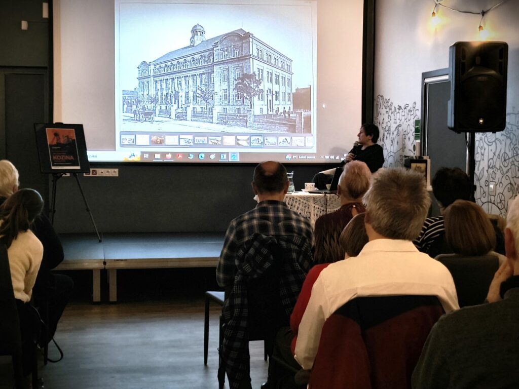 Prof. Irma Kozina stoi koło ekranu, na ekranie zdjęcie budynku