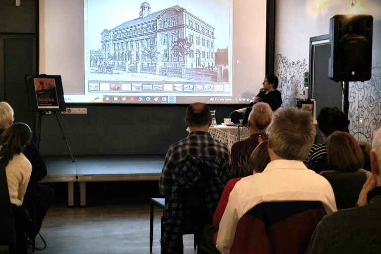 Prof. Irma Kozina stoi koło ekranu, na ekranie zdjęcie budynku