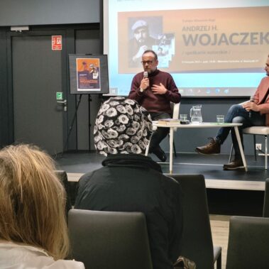 Na scenie siedzą Andrzej H. Wojaczek i prowadzący spotkanie Jakub Strumień