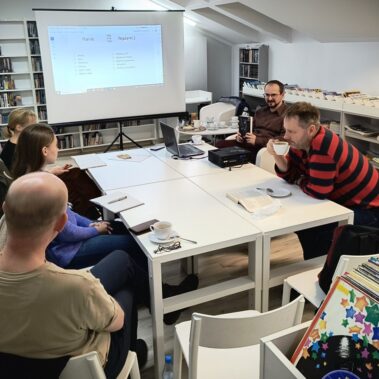 Widok ogólny na warsztaty literackie, jeden z panów pije kawę