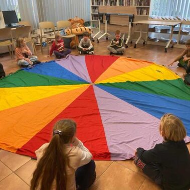 Dzieci siedzą wokół kolorowej płachty