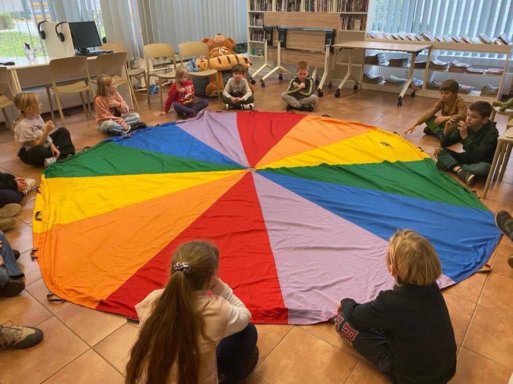 Dzieci siedzą wokół kolorowej płachty