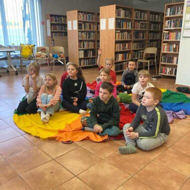 Dzieci siedzą na kolorowej płachcie