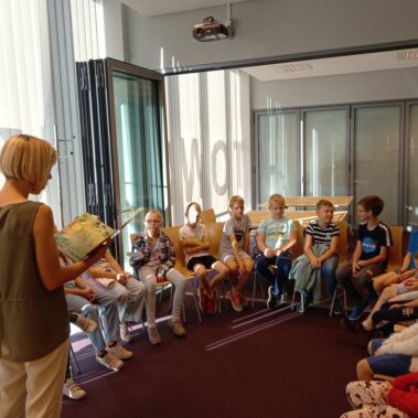 Dzieci siedzą na krzesłach i słuchają głośnego czytania