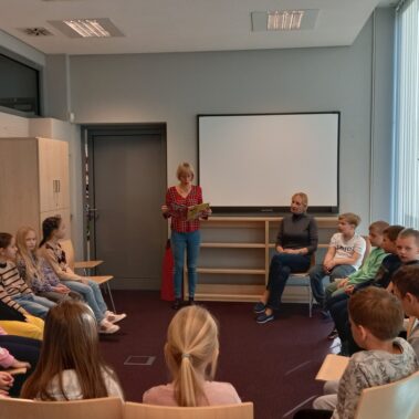 Bibliotekarka głośno czyta książkę, dzieci słuchają