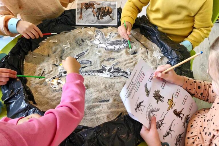 Dzieci bawią w paleontologów, wygrzebują szczątki z piasku i opisują