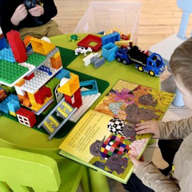 Chłopiec przegląda książkę o słoniu Elmera, na stole leżą klocki Lego Duplo
