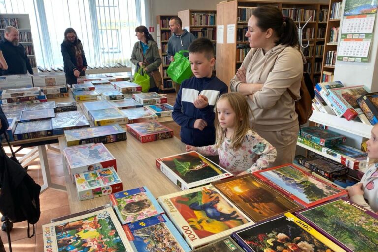 Uczestnicy przy stole z ułożonymi pudełkami z puzzlami