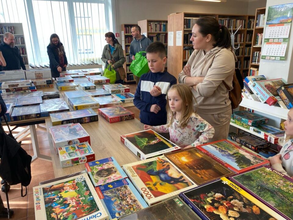 Uczestnicy przy stole z ułożonymi pudełkami z puzzlami