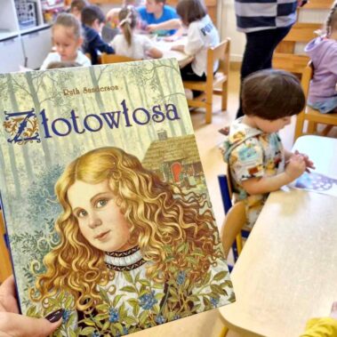 Okładka książki – Złotowłosa – Ruth Sanderson, w tle dzieci przy pracy plastycznej