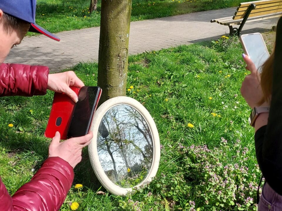 Uczestnicy robią zdjęcia w stronę owalnego lustra z odbiciami drzew.