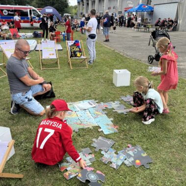 Dzieci w towarzystwie ojca układają puzzle na trawniku