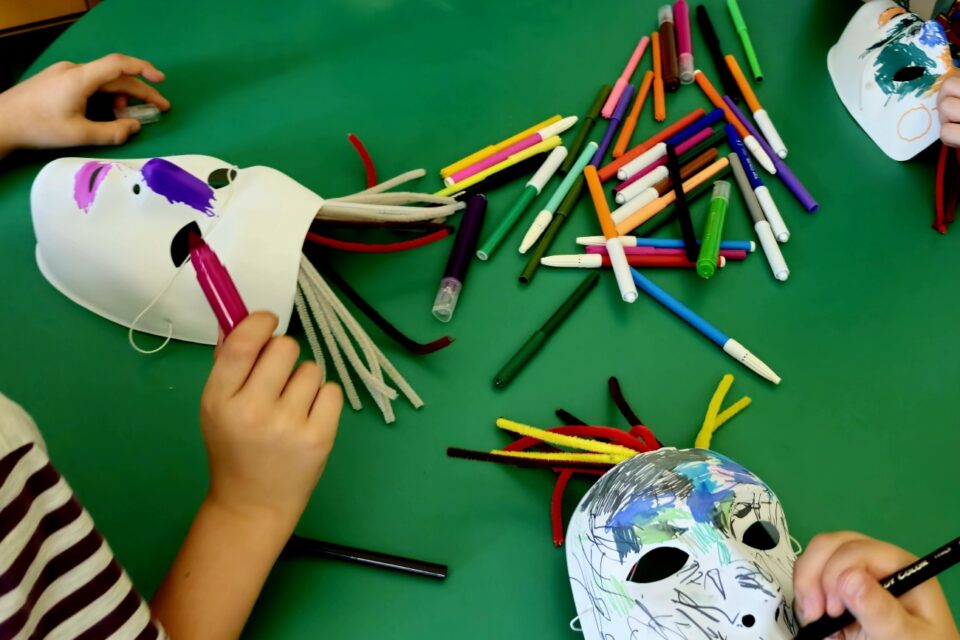 Na stole leżą maski i mazaki i ręce przy pracy