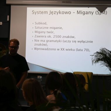 Za lektorem jest wyświetlany slajd o Systemie Językowo - Migany
