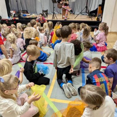Widok ogólny, dzieci siedzą, a scenie grają panie