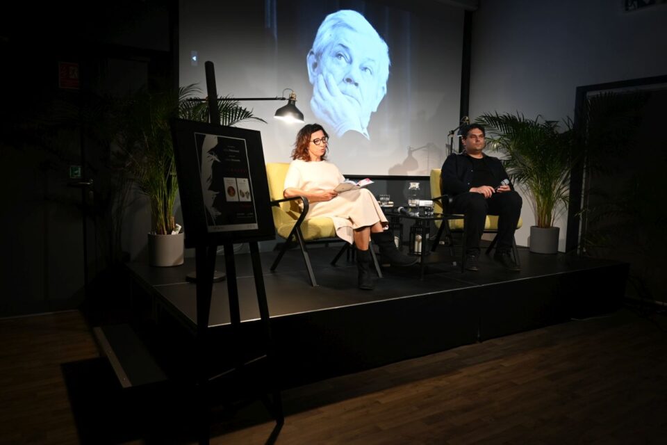 Na scenie siedzą Jolanta Olszewska i Juliusz Pielichowski. Na ekranie wyświetla się zdjęcie Zbigniewa Herberta