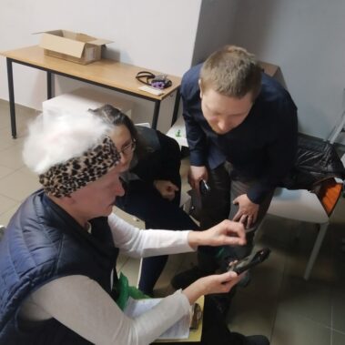 Starsza pani pokazuje uczestnikom zdjęcia na smartfonie