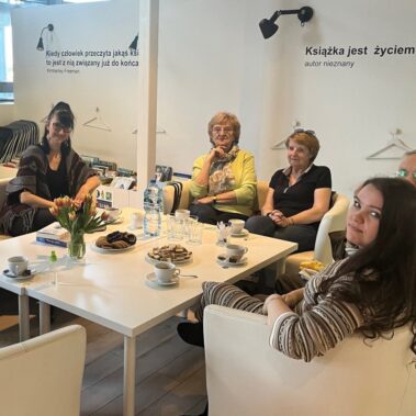 Przy stole siedzą seniorzy i bibliotekarki.
