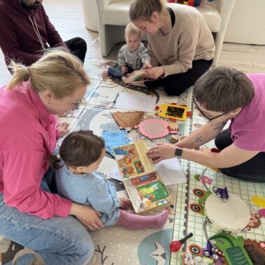 Rodzice z dziećmi i bibliotekarką przeglądają książki