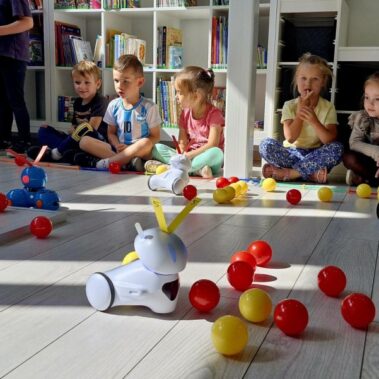 Na podłodze poruszają roboty popychając kulki, dzieci obserwują