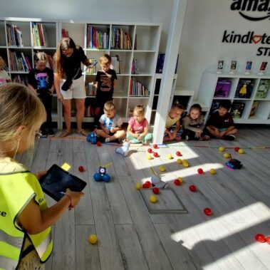 Dwie drużyny rywalizują sterując robotami, Na pierwszym planie dziewczyna obsługuje tableta