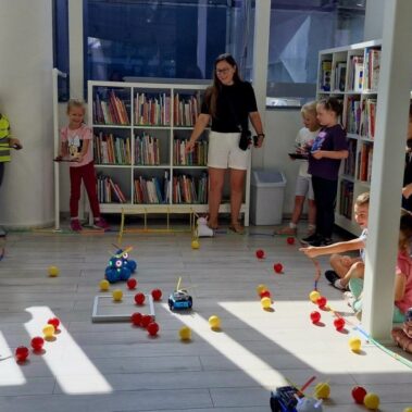 Dwie drużyny rywalizują sterując robotami. Po podłodze roboty poruszają pchając kulki.