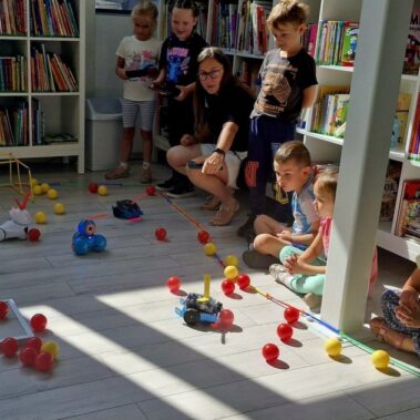 Dwie drużyny rywalizują sterując robotami. Po podłodze roboty poruszają pchając kulki. W akcjj niebieski mBot2.