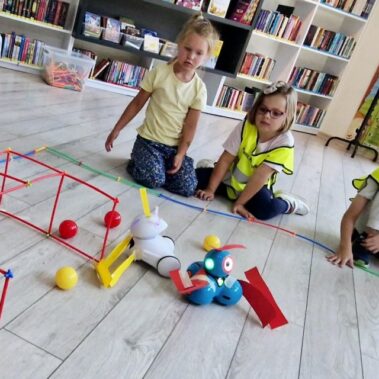 Robot Photon z chwytakiem w stylu spychacza pcha piłkę do bramki. dzieci obserwują. Bramkę broni drugi robot.