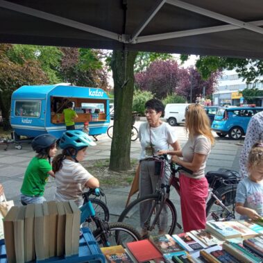 Bibliotekarka rozmawia z czytelnikami, którzy przyjechali rowerami i inni czytelnicy przeglądają stoisko
