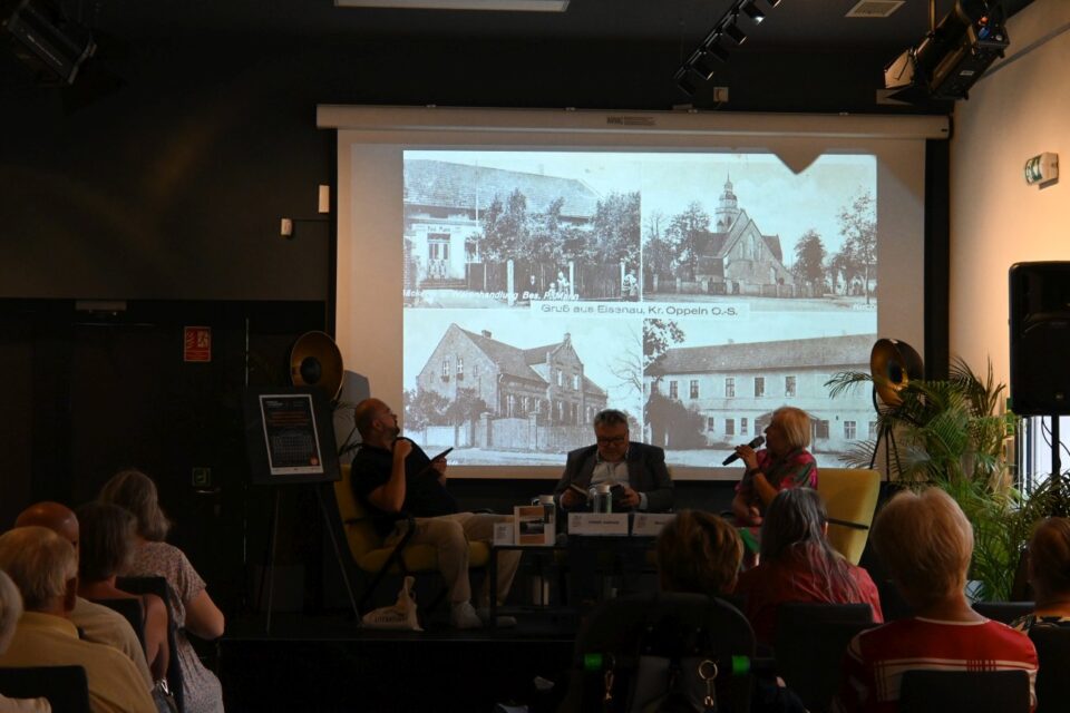 Na ekrane jest wyświetlany stare zdjęcia wsi Eisenau - Żelaznej (powiat opolski), na scenie siedzą prelegenci.