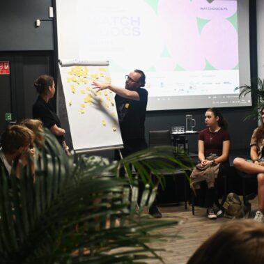 Warsztaty, Prowadzący wyjaśnia o nalepkach na tablicy, młodzież słuchają
