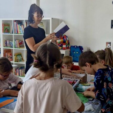 Bibliotekarka czyta na głos książkę, a dzieci wykonują prace plastyczne