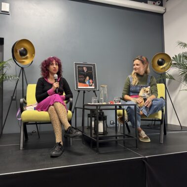 Na scenie siedzą Sylwia Chutnik i Maria Hawranek, u jej siedzi piesek